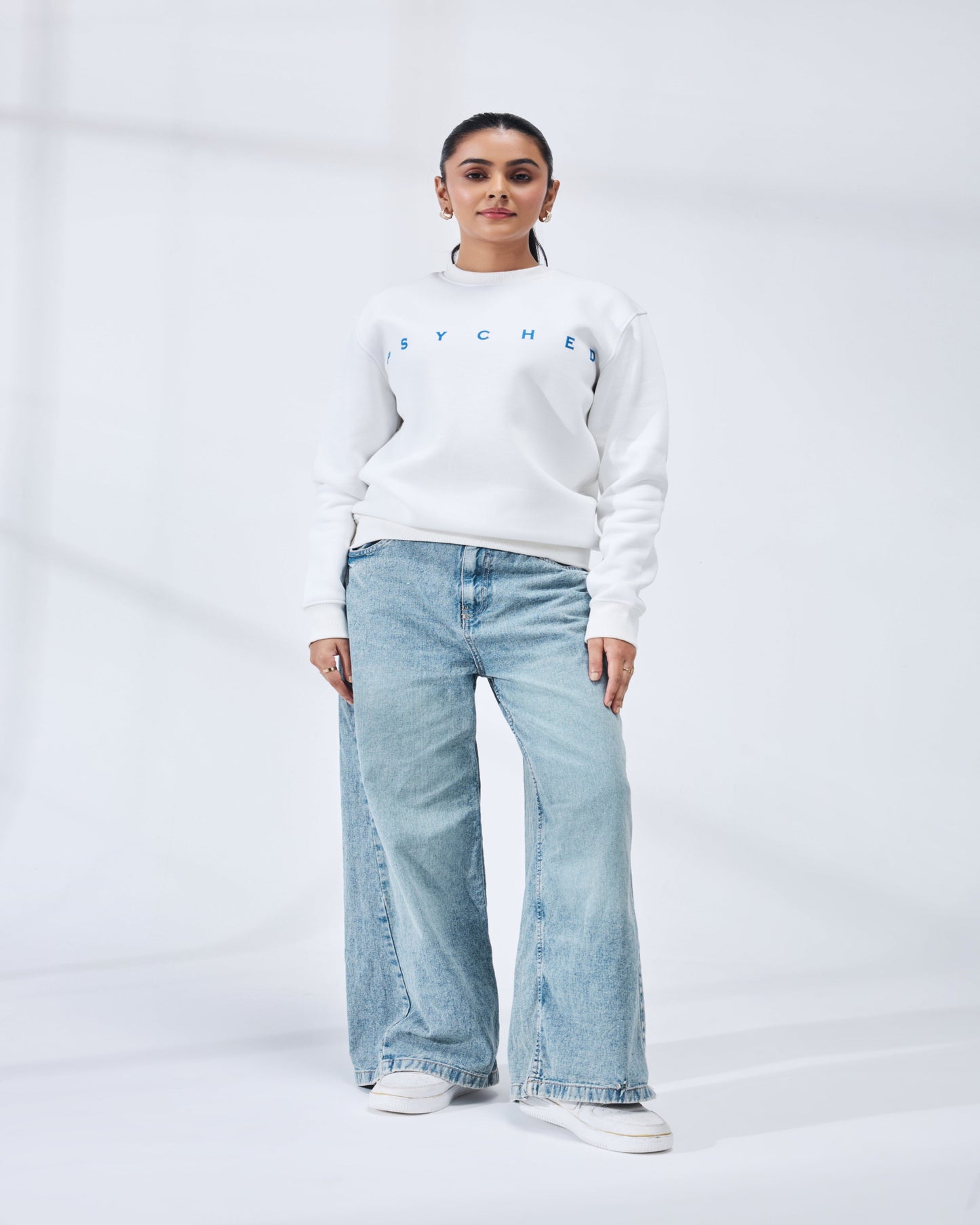 Person wearing a white sweatshirt with text and light blue jeans on a white background