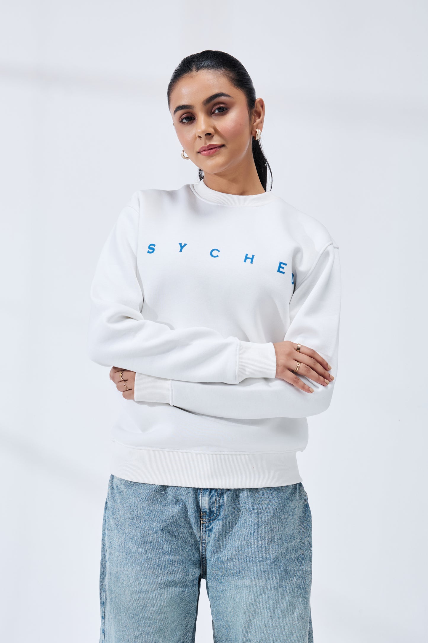 Woman wearing a white sweatshirt with 'SYCHE' branding against a plain background