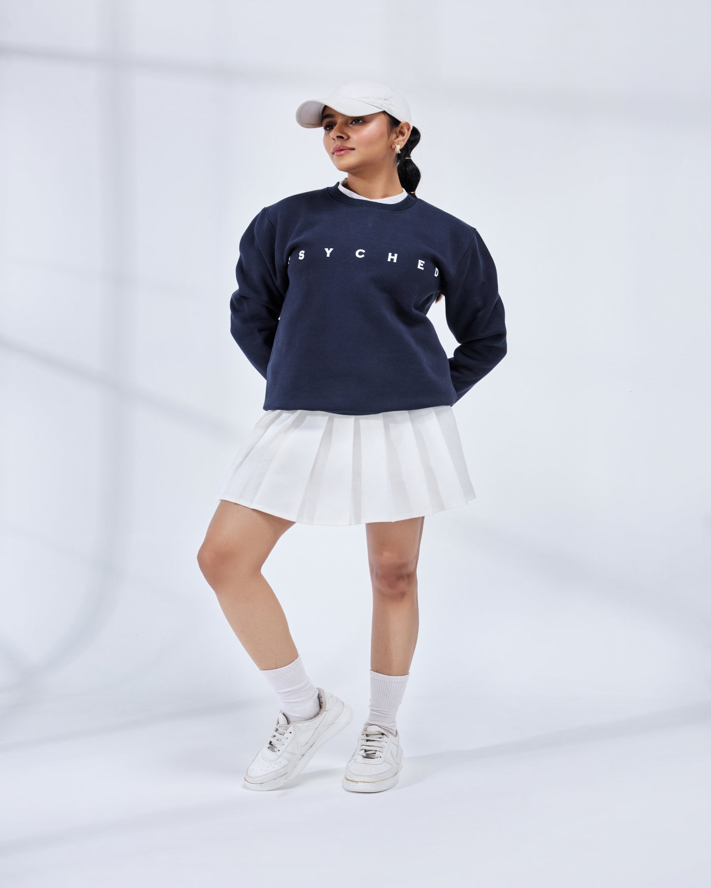 Person wearing a navy blue sweatshirt with 'HYPER' text, white skirt, and white sneakers on a light gray background