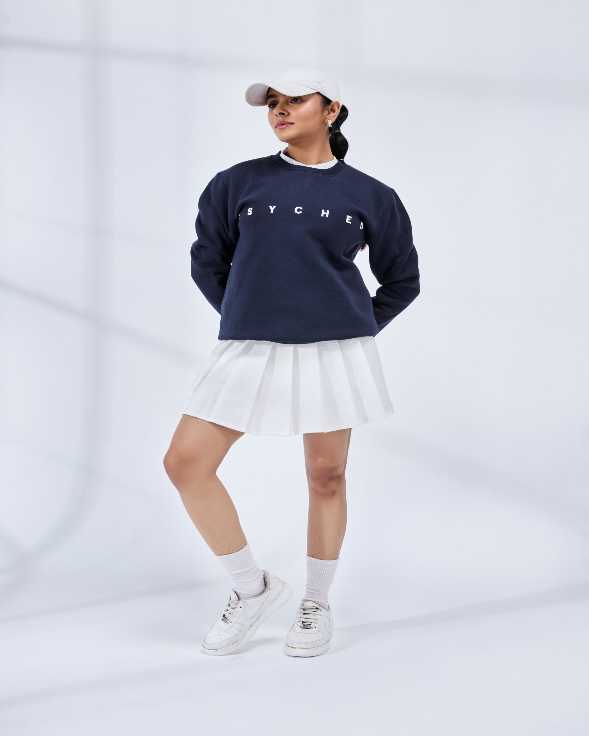 Person wearing a navy blue sweatshirt with 'HYPER' text, white skirt, and white sneakers on a light gray background