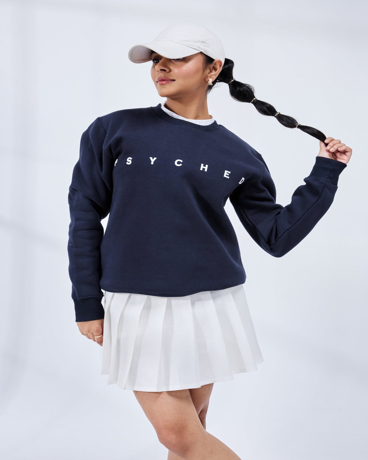 Person wearing a navy blue sweatshirt with 'SYCHE' branding and a white skirt on a light gray background