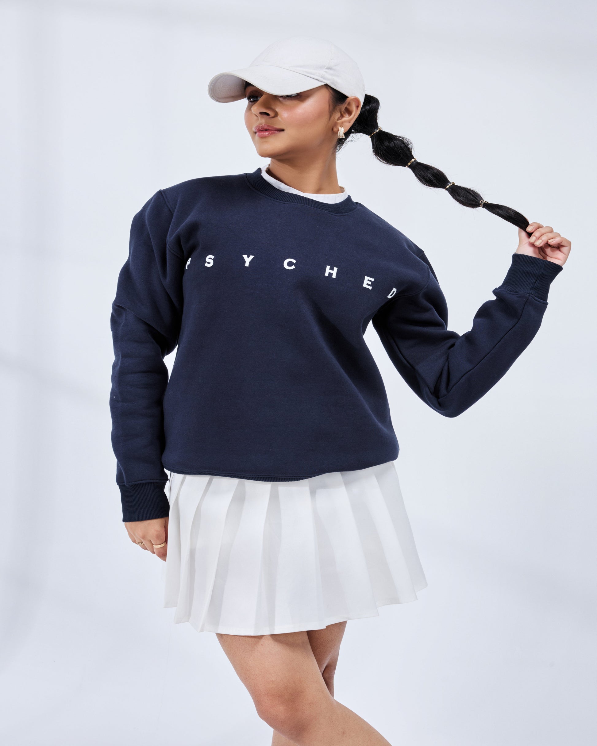 Person wearing a navy blue sweatshirt with 'SYCHE' branding and a white skirt on a light gray background
