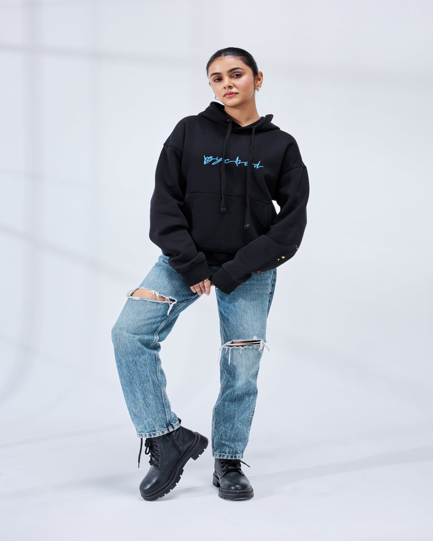 Person wearing a black hoodie with blue text and ripped jeans on a white background