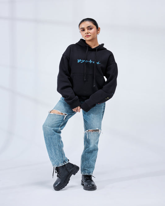 Person wearing a black hoodie with blue text and ripped jeans on a white background