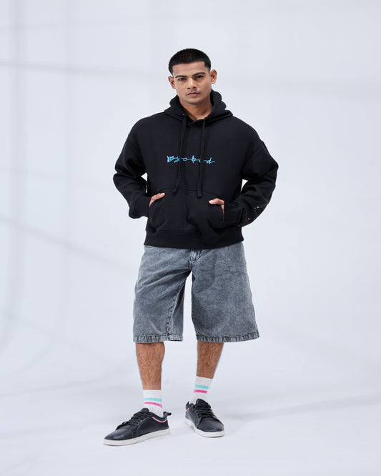 Person wearing a black hoodie with blue text and gray shorts on a white background