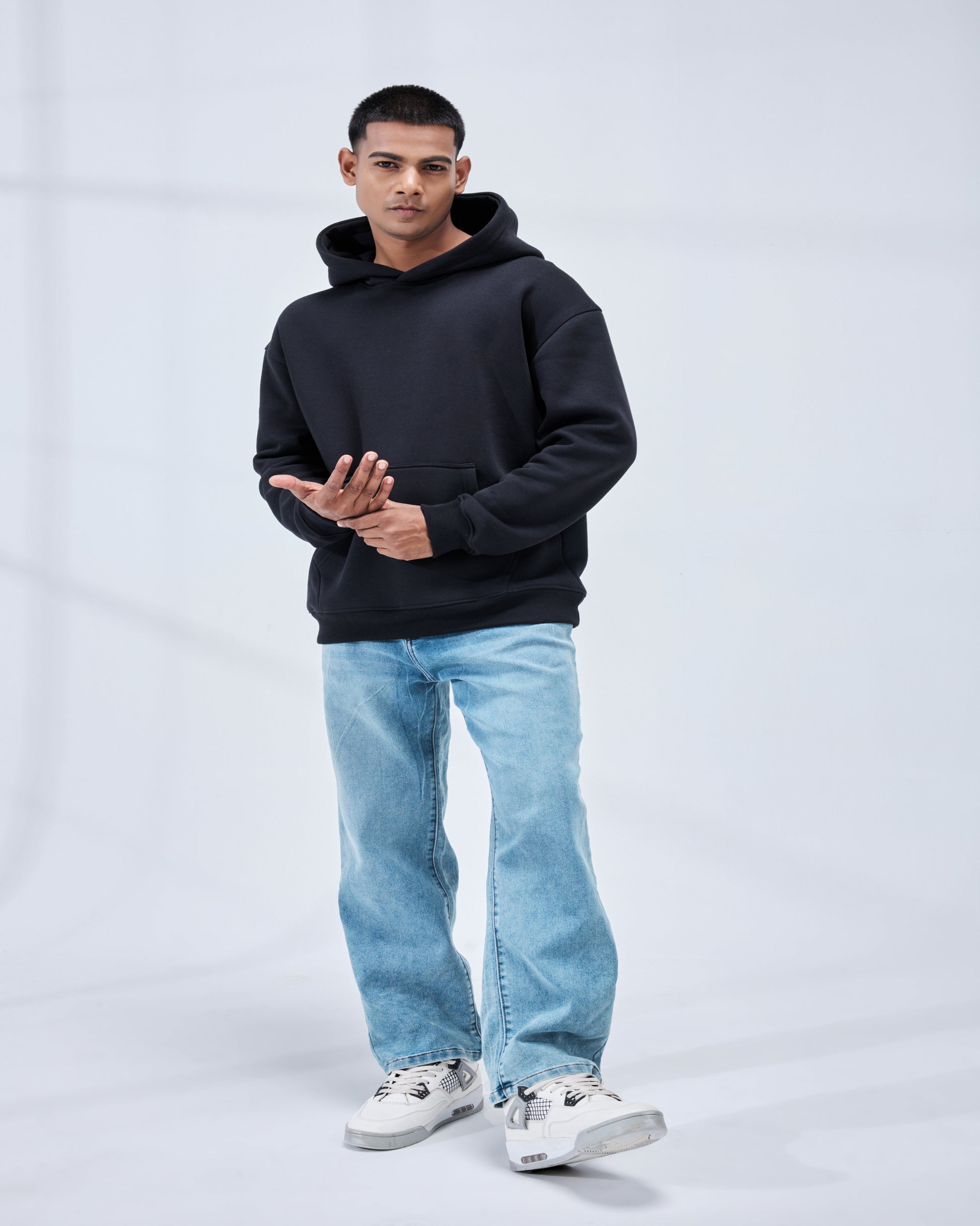 Man wearing a black hoodie and light blue jeans on a white background