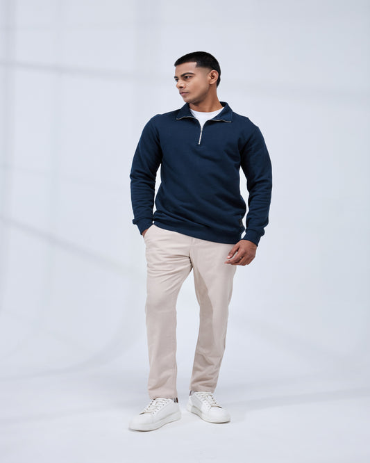Man wearing a navy blue pullover with a white collar, beige pants, and white sneakers on a light gray background