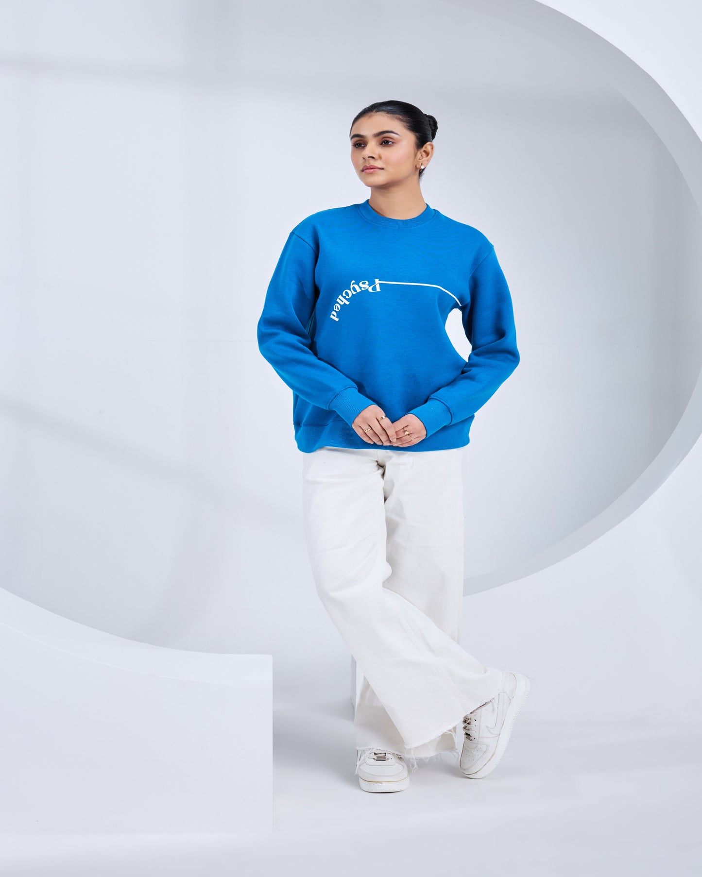 Person wearing a blue sweater with text and white pants on a light gray background