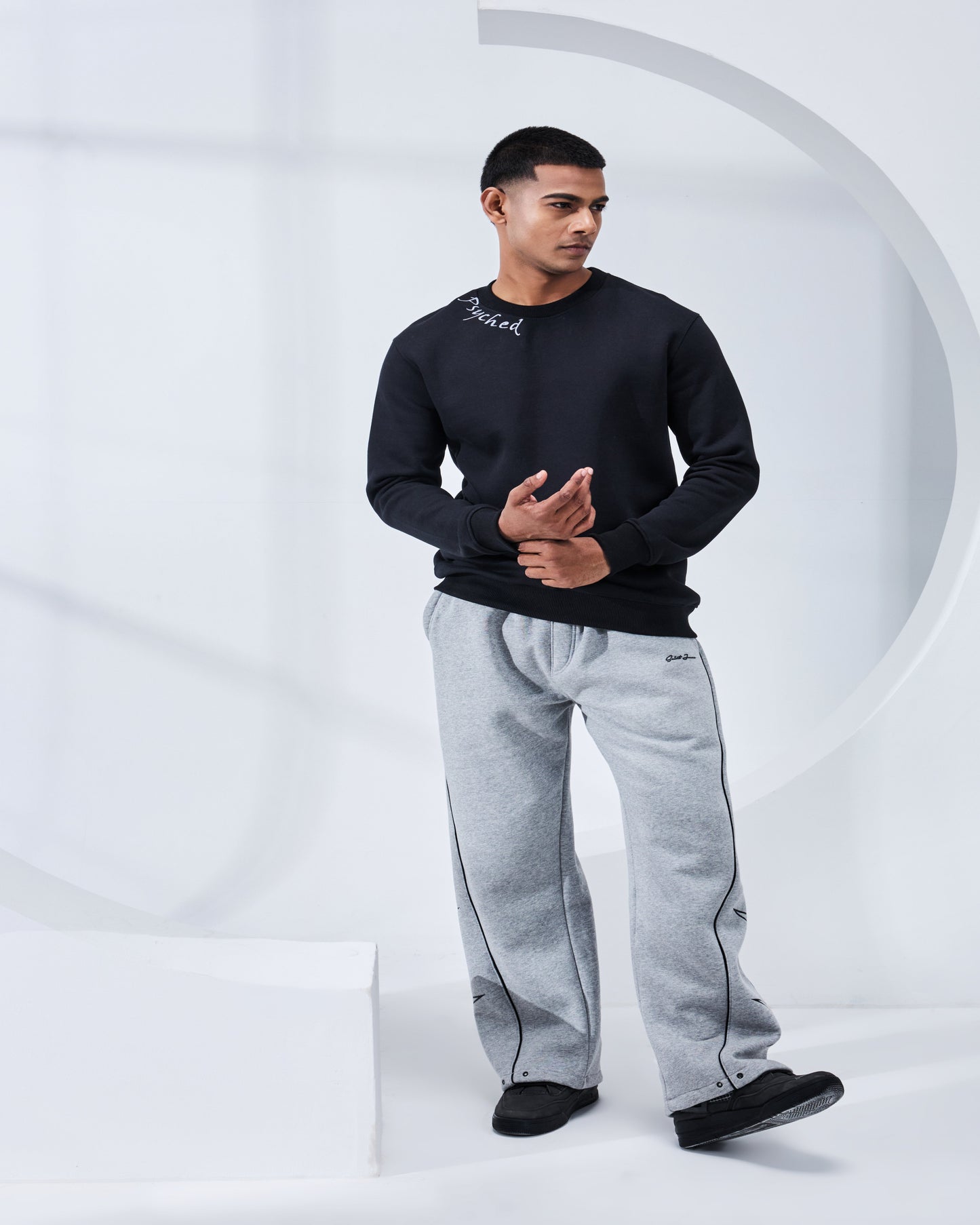 Person wearing a black long-sleeve shirt and gray sweatpants on a white background