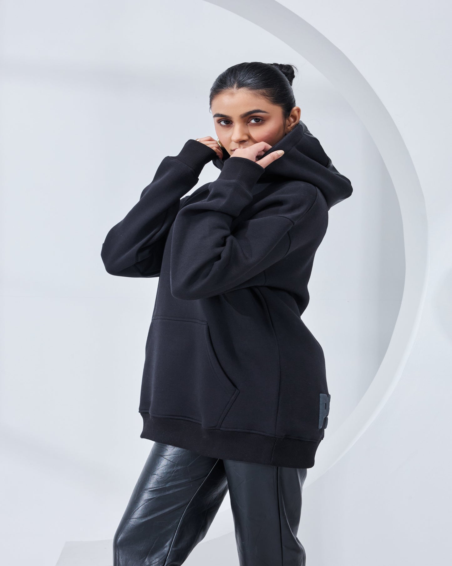 Person wearing a black hoodie and black pants against a white background
