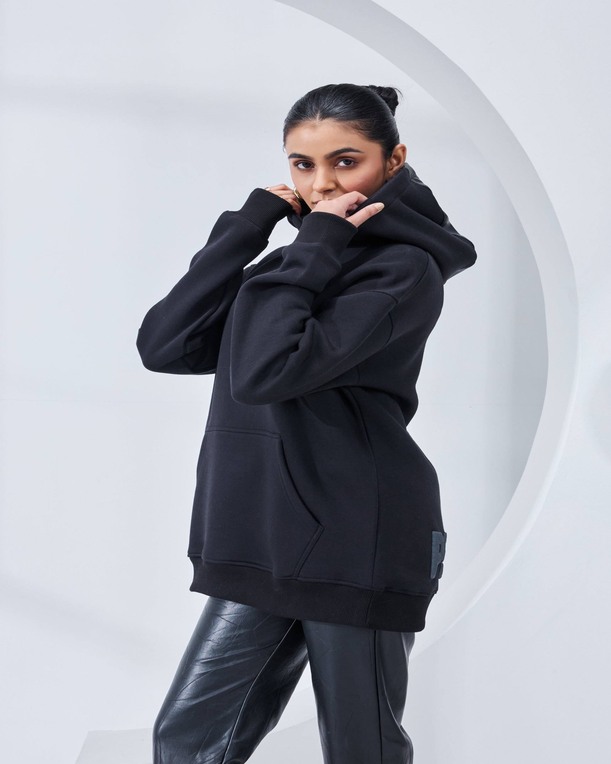 Person wearing a black hoodie and black pants against a white background